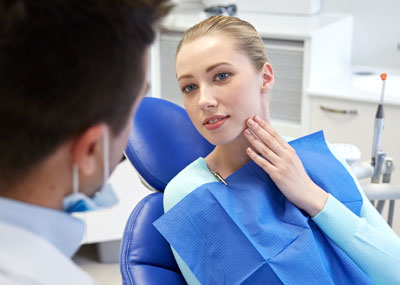 woman sitting in front of dentist touching her jaw